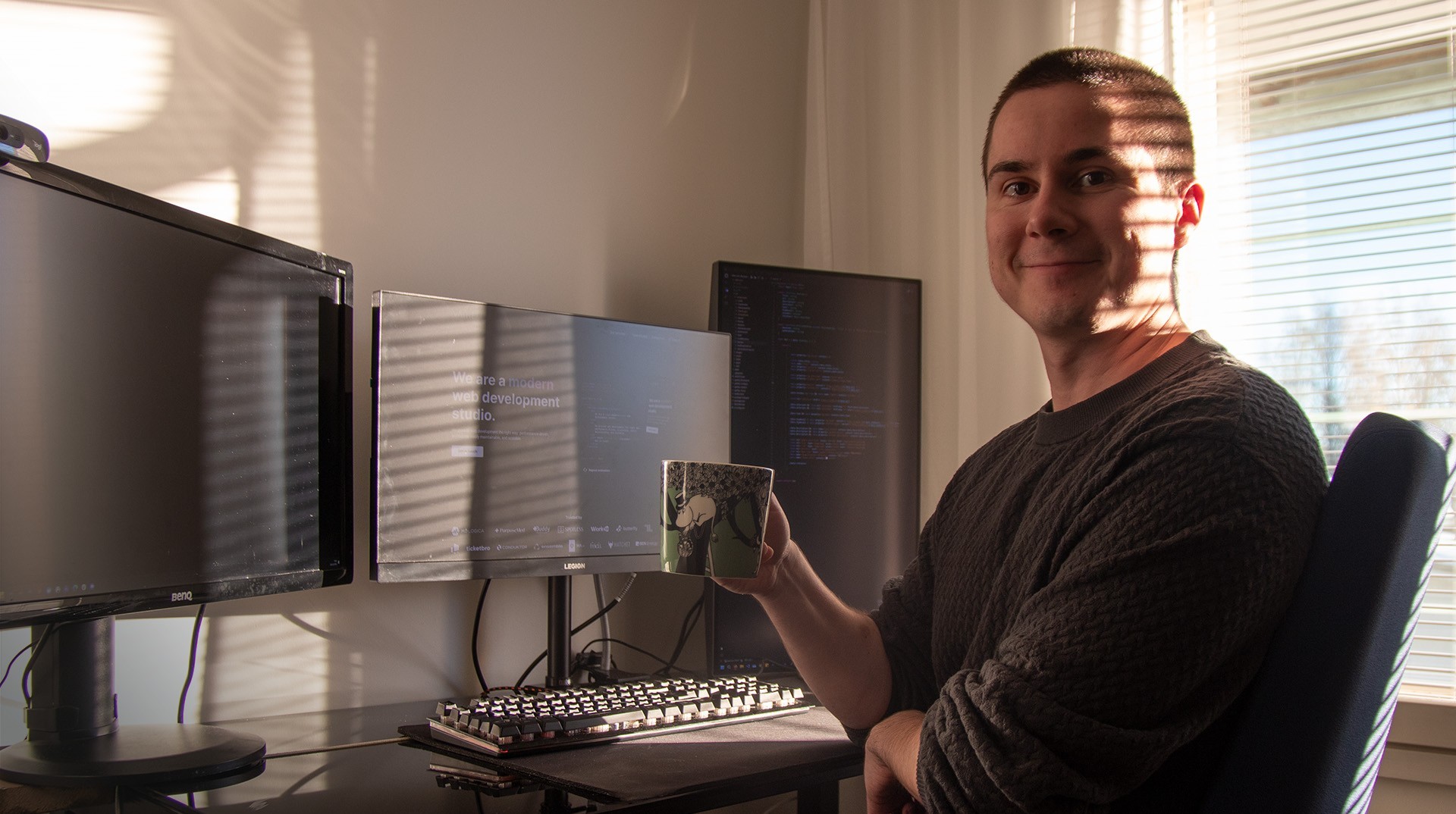 Jere sitting at his desk, holding a mug in front of his computer monitors